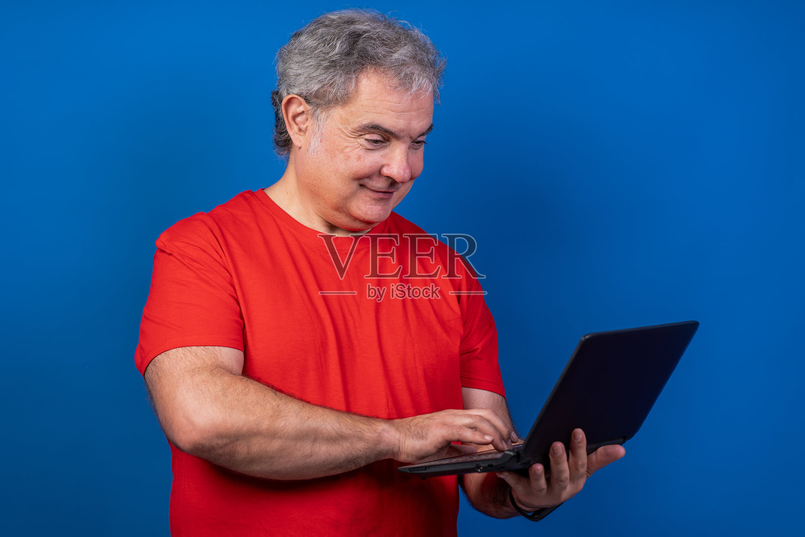 一名穿着红色衬衫的男子微笑着手持一台笔记本电脑照片摄影图片