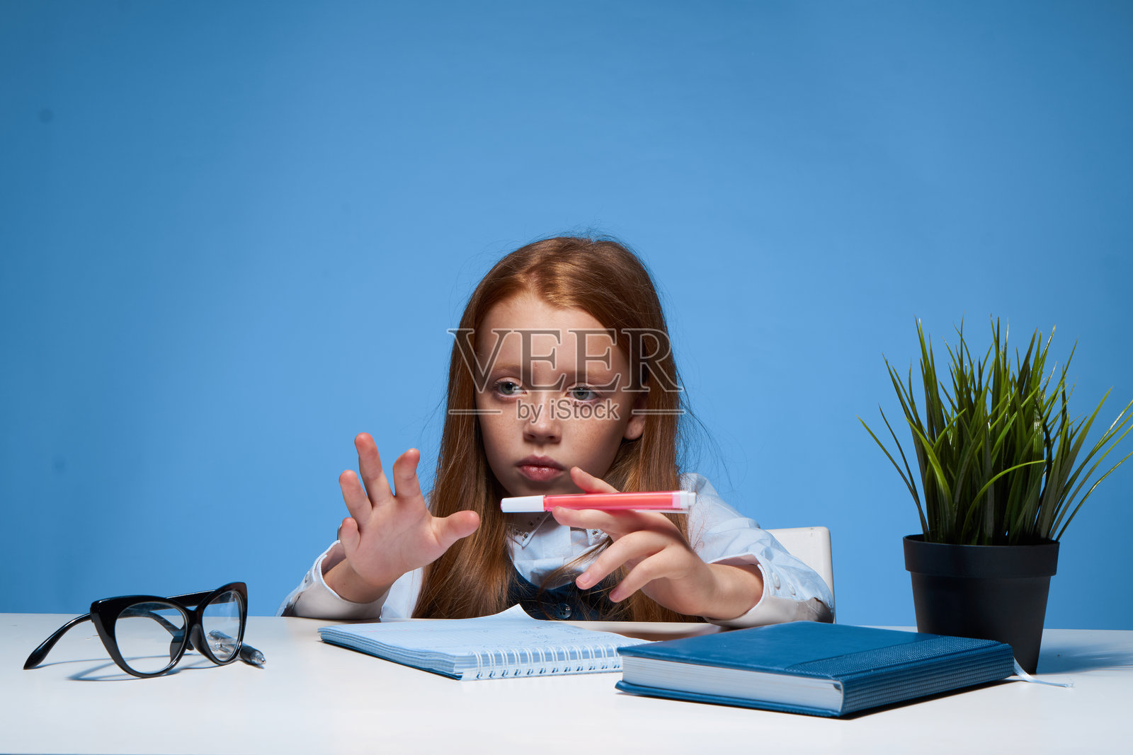 红发女孩坐在桌子旁，面前摆着教科书，正在学习。照片摄影图片