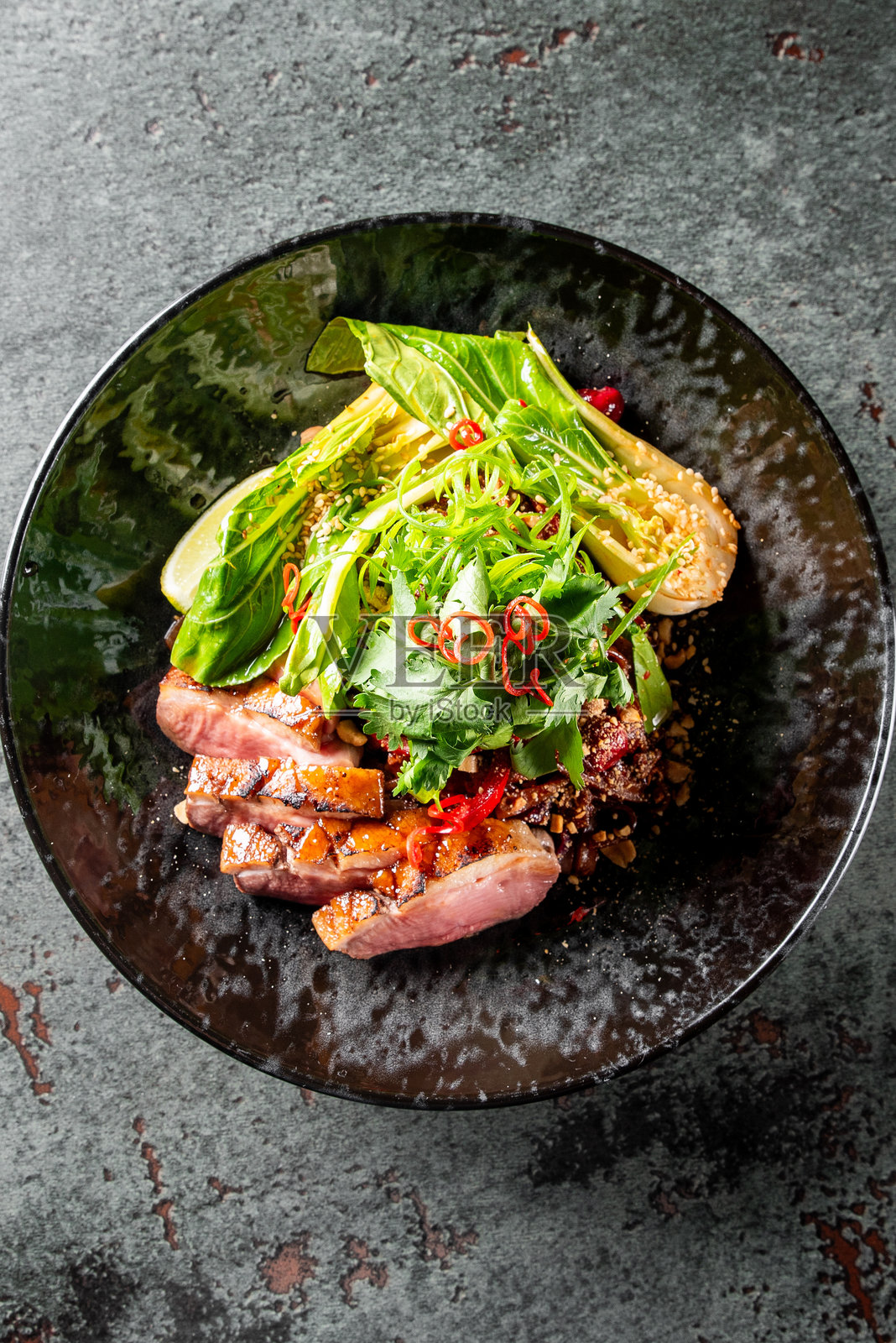 一道色彩鲜艳的菜肴，盘中有切片的烤肉、新鲜的绿叶、芝麻和辣椒，搭配一个柠檬角，放在深色盘子上。非常适合食品摄影、烹饪博客和餐厅推广。照片摄影图片