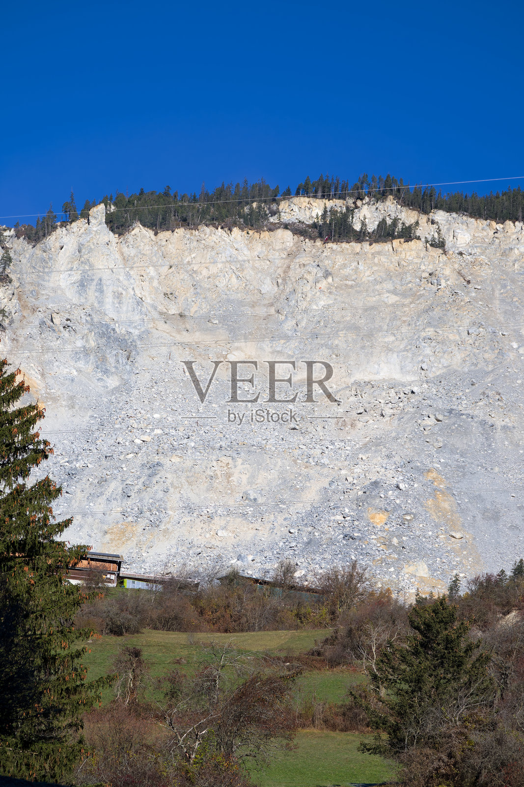 瑞士阿尔卑斯山布伦扎乌斯山村的岩石滑落，直升机和工人悬挂在绳索上安装镜子，背景是晴朗的蓝天，秋日阳光明媚。照片摄影图片