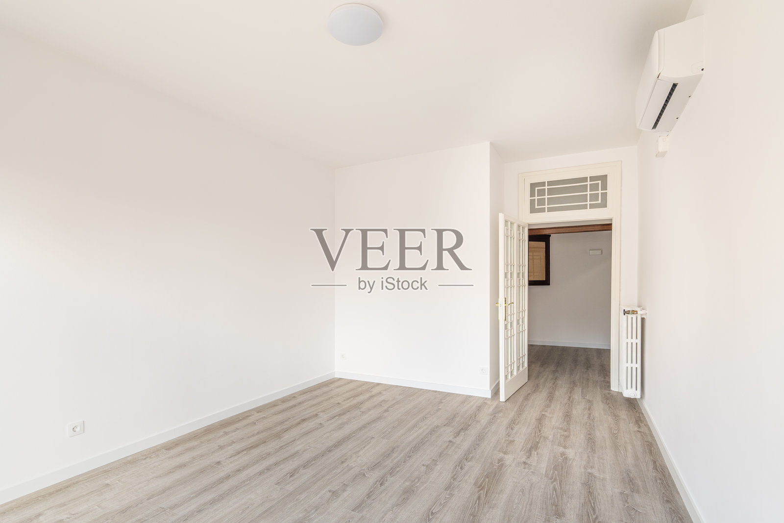 一个宽敞的空房间作为卧室，墙上有空调和散热器以在寒冷季节提供暖气。环保木地板。照片摄影图片