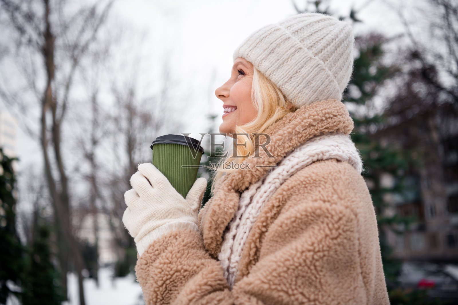 可爱的女士穿着米色外套，在城市公园户外喝热可可。照片摄影图片