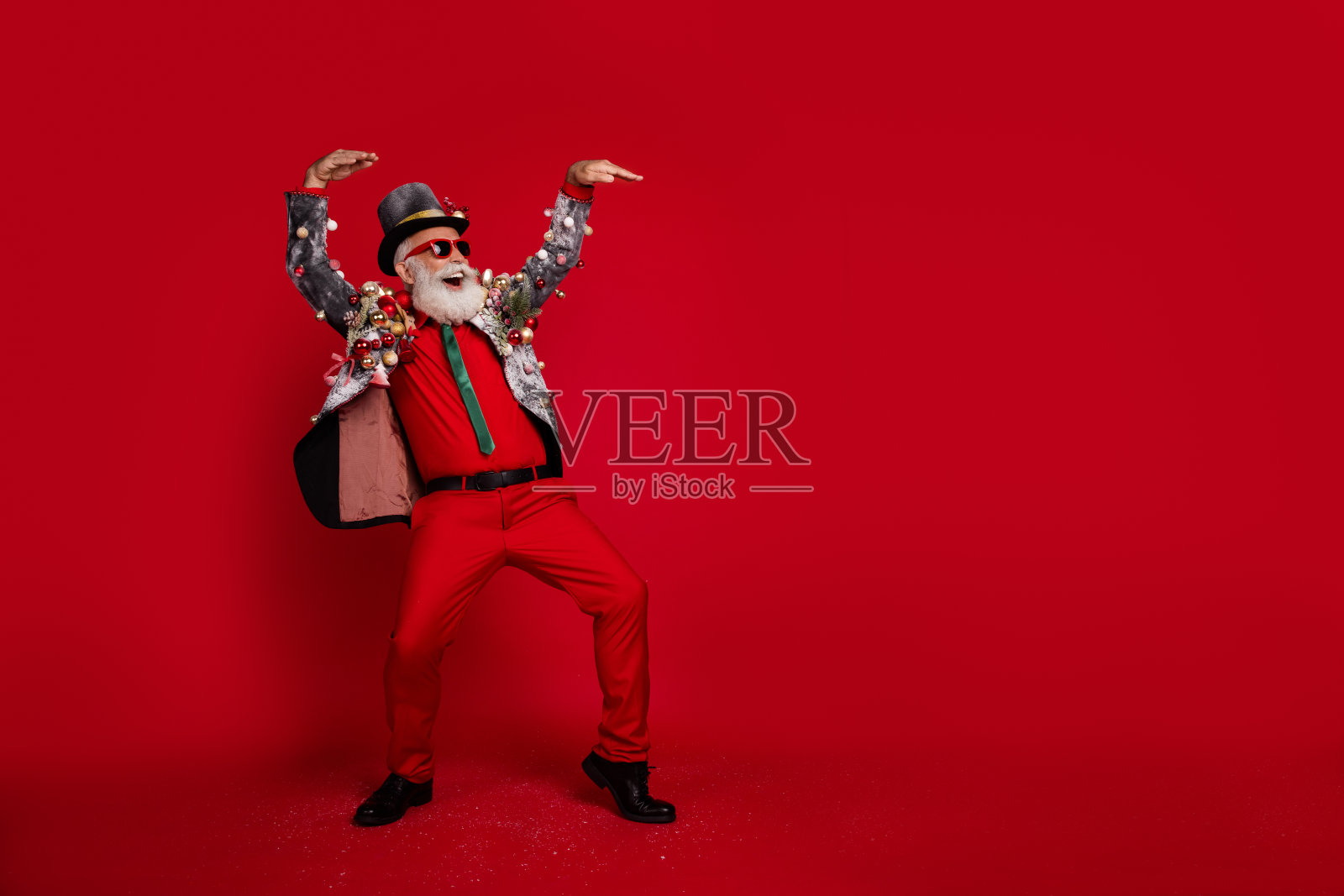 穿着圣诞服装的时尚酷爷爷在空旷的红色背景下尽情享受圣诞节的乐趣。照片摄影图片
