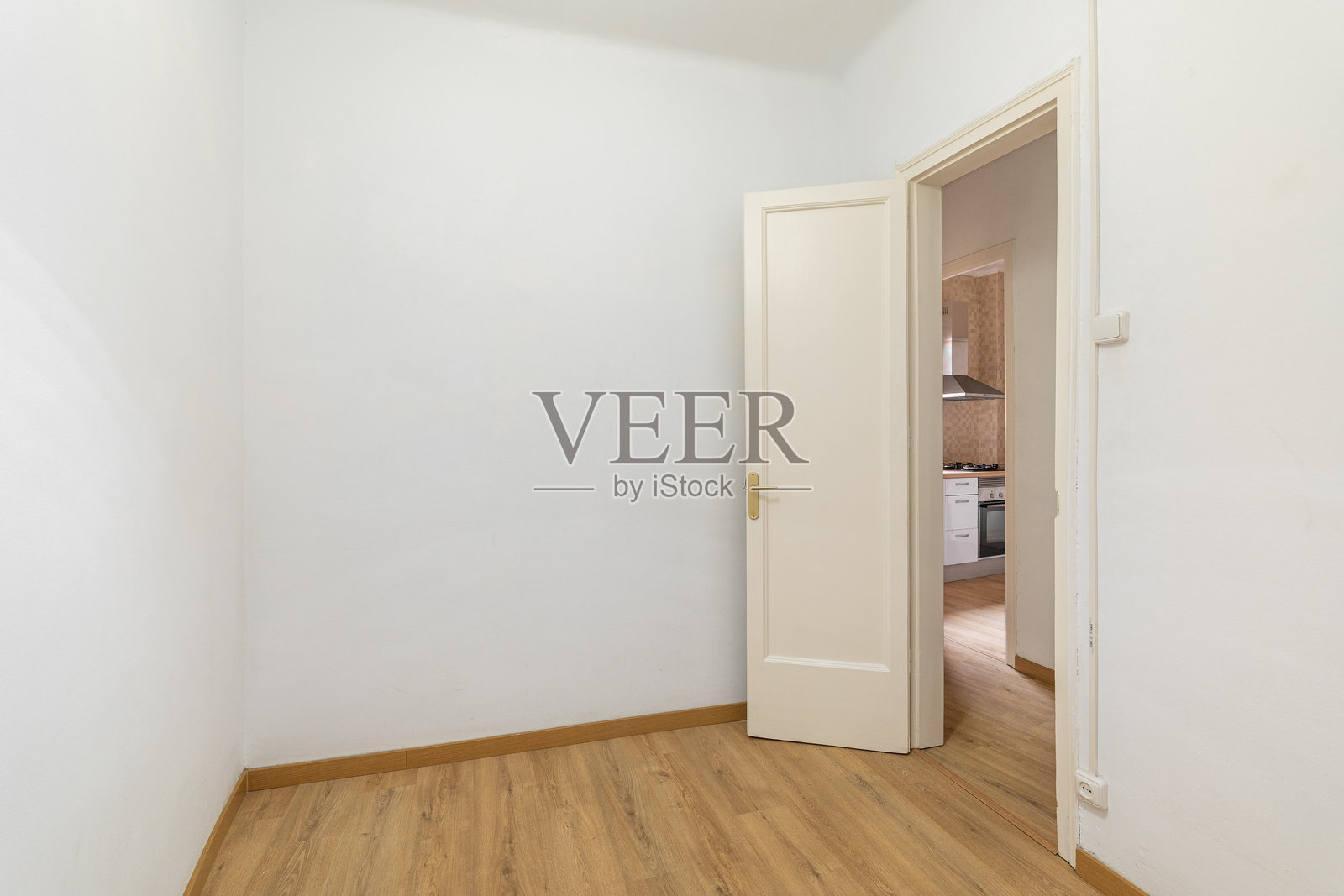 空荡荡的白色房间，前面有一扇门，透过门可以看到一个温馨的厨房，地面铺有木质层压板，位于一间新公寓中。准备布置和乔迁的概念。留白空间。照片摄影图片