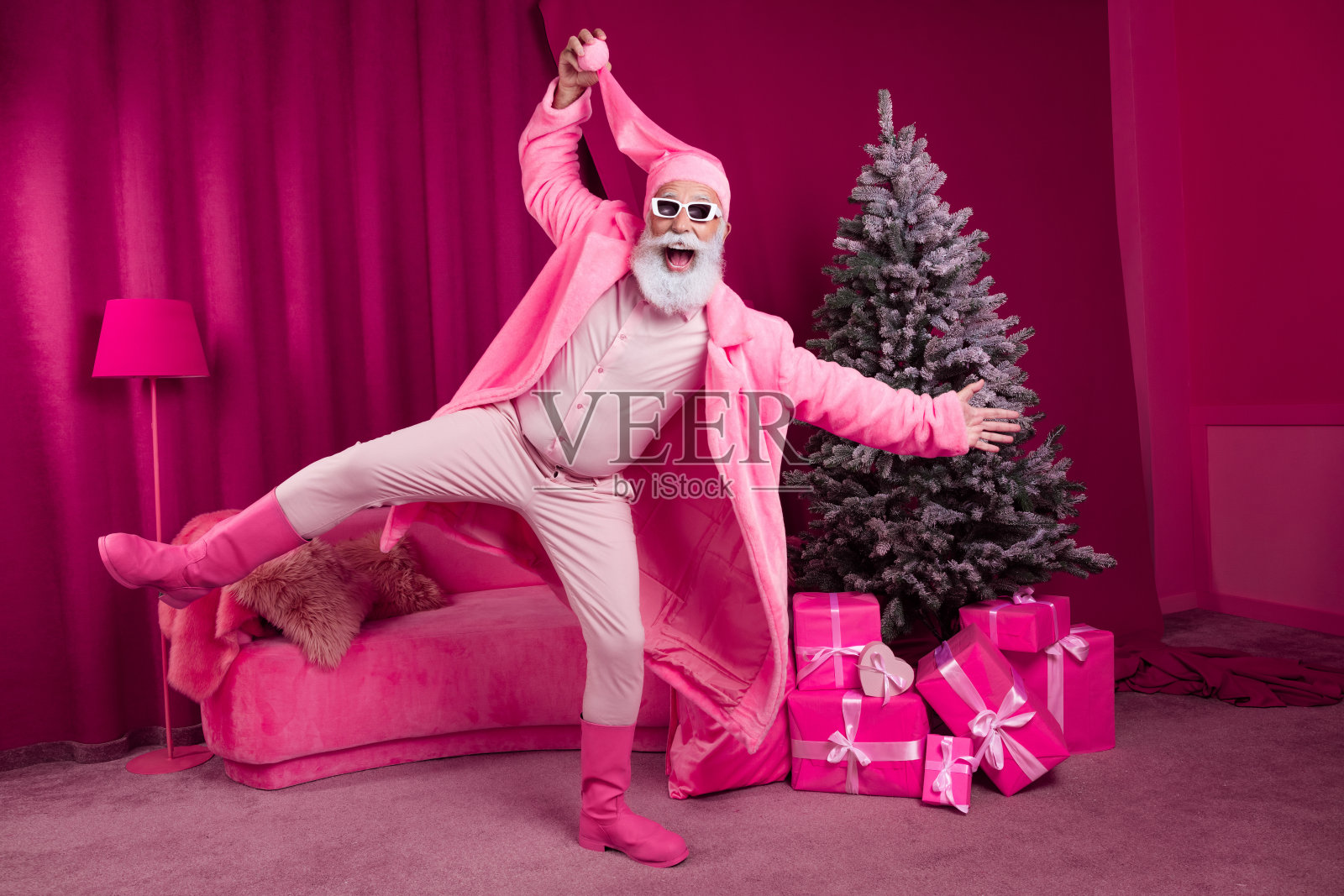 穿着酷炫靴子和毛皮外套的时尚老年胡子圣诞老人，戴着蓬松的睡帽，庆祝粉色新年装饰的圣诞节。照片摄影图片