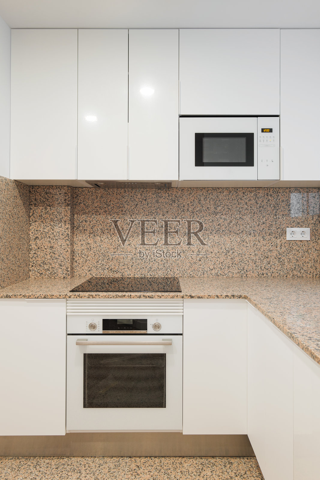 现代厨房通过滑动窗户的自然光照亮。米色花岗岩墙面上有黑色斑点。厨房家具由木材制成，表面涂有白色光泽漆。内置现代科技。照片摄影图片