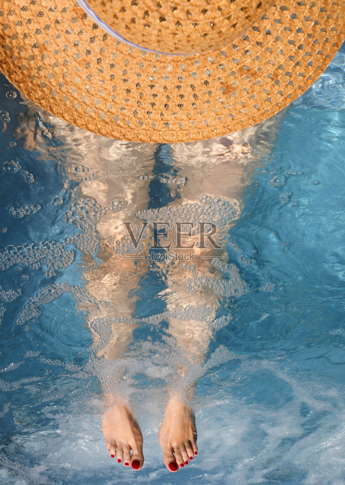从空中俯瞰一位戴着大草帽、长腿的女性在游泳池中。照片摄影图片