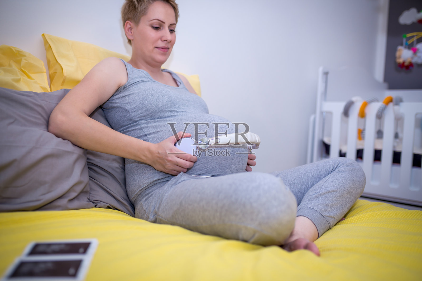 孕妇在床上放松，耳机放在大肚子上。照片摄影图片