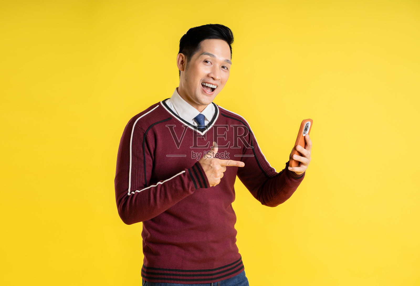 穿着圣诞毛衣的亚洲男子在黄色背景下使用手机的肖像照片摄影图片