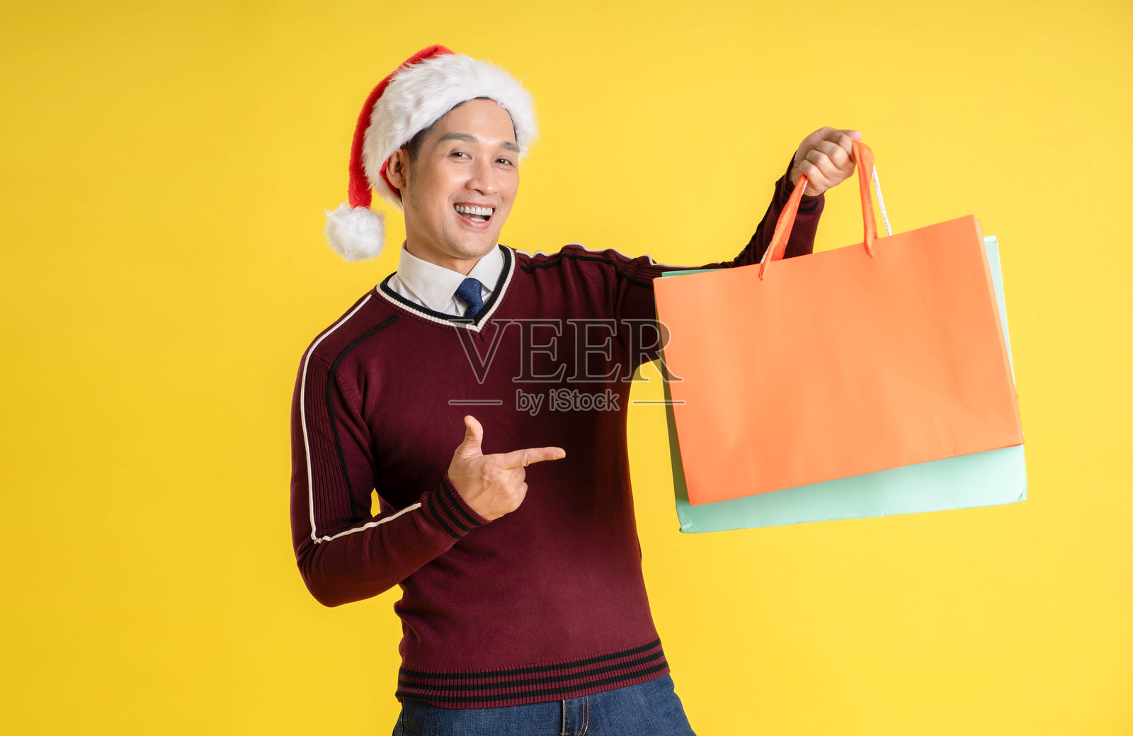 穿着圣诞毛衣和帽子的亚洲男子在黄色背景下手持购物袋的肖像照片摄影图片
