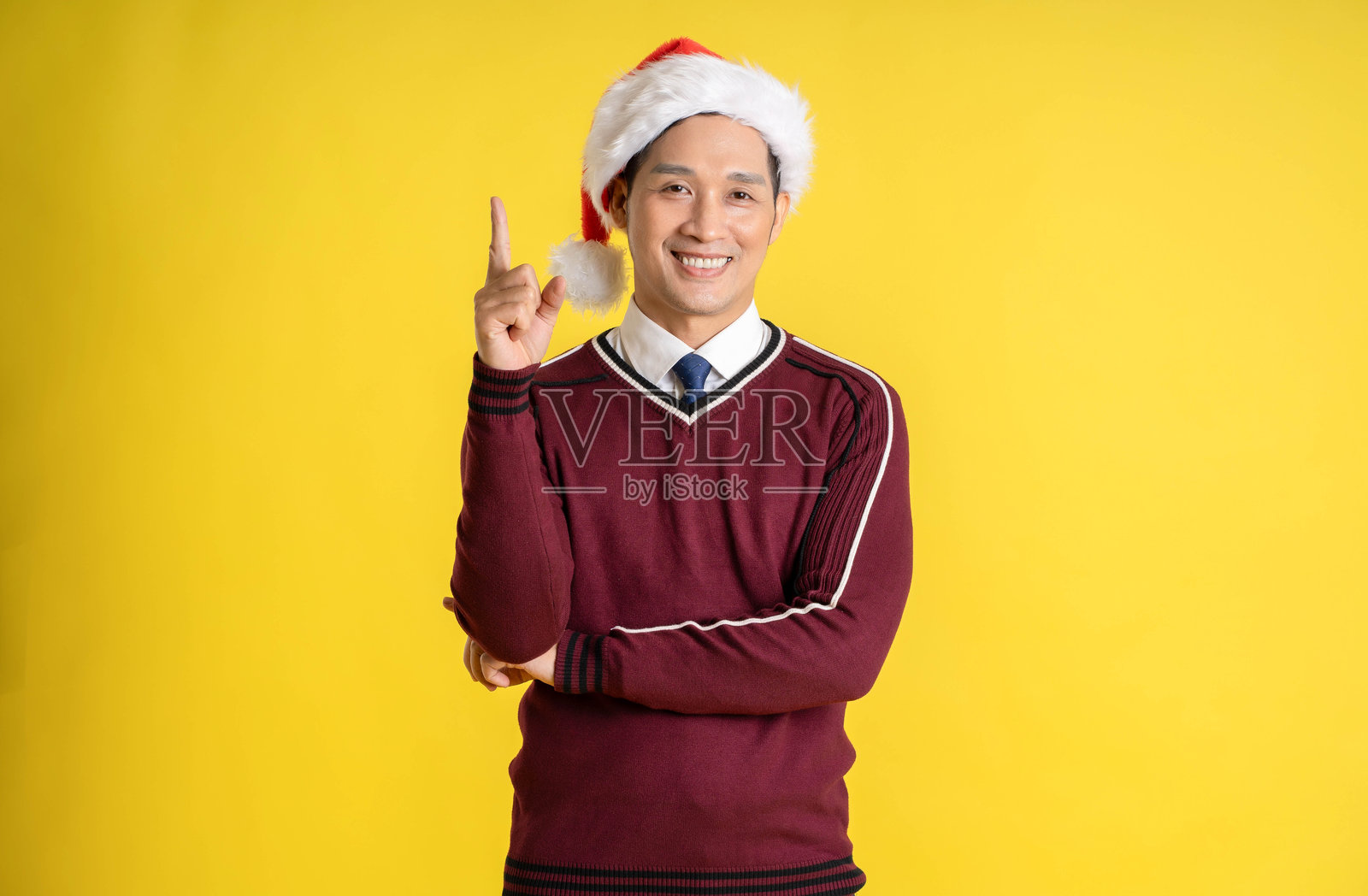 穿着圣诞毛衣和帽子的亚洲男子在黄色背景前摆姿势的肖像照片摄影图片