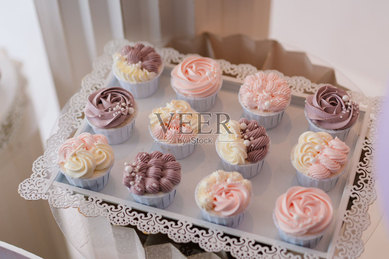 装饰有淡色花朵形状奶油的杯子蛋糕，整齐地摆放在白色托盘上。生日派对概念。照片摄影图片