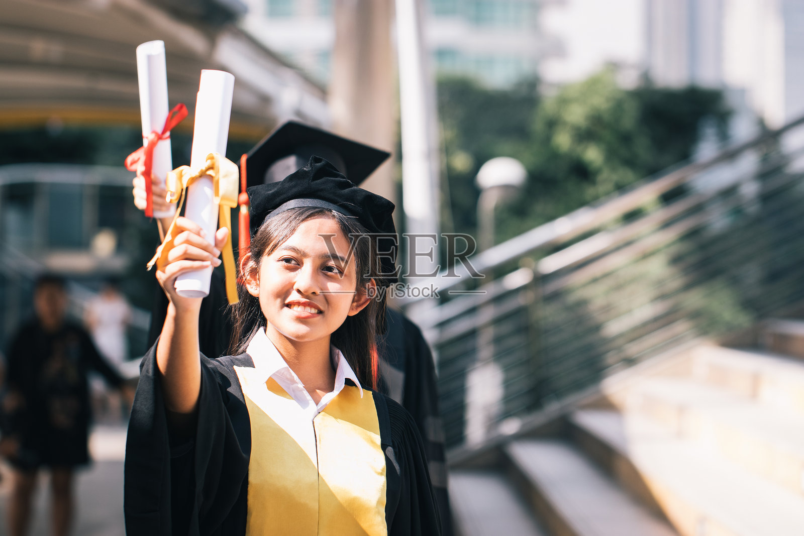 穿着毕业袍的少女在户外手持证书站立照片摄影图片