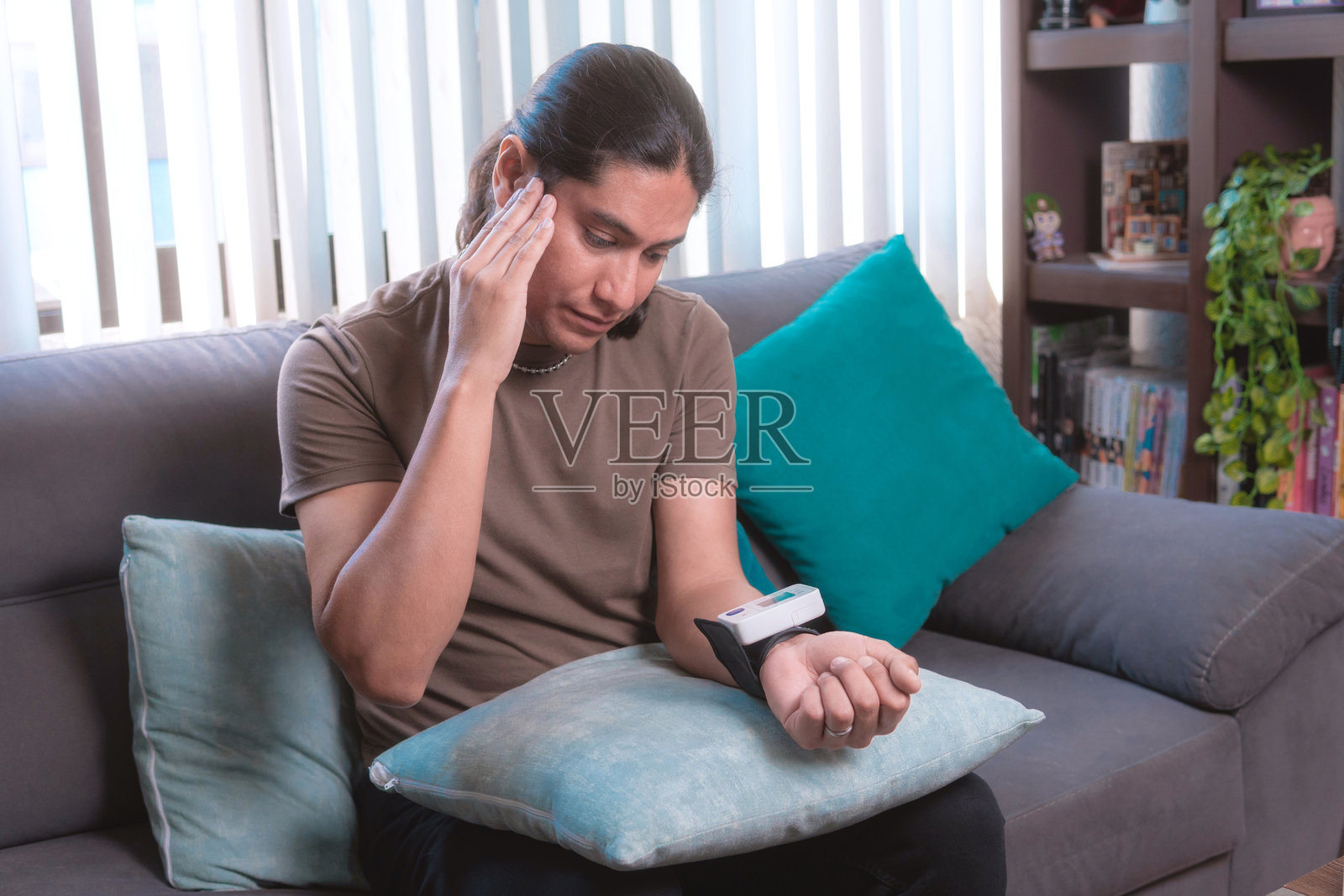 一位中年男子坐在家里的沙发上，手中拿着便携式血压监测仪检查自己的血压。照片摄影图片