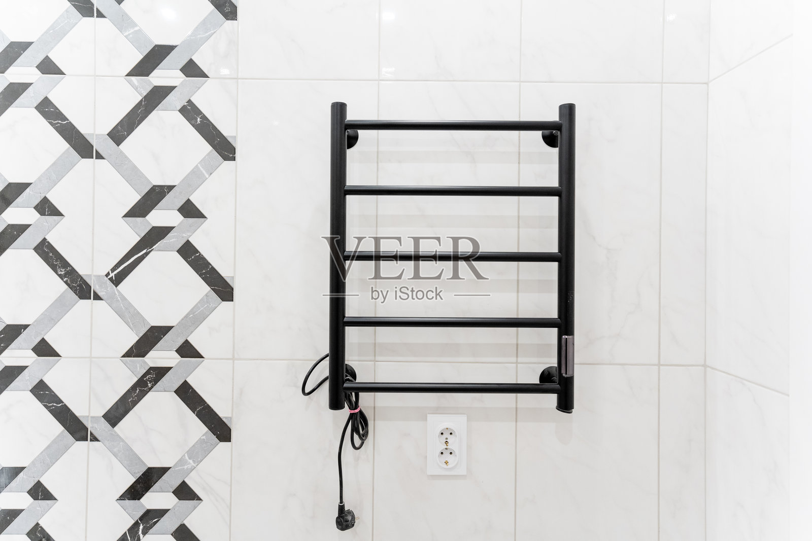 一款光滑的黑色毛巾架优雅地悬挂在浴室洁白的瓷砖墙上，为整个空间的设计和功能增添了一丝现代感。照片摄影图片