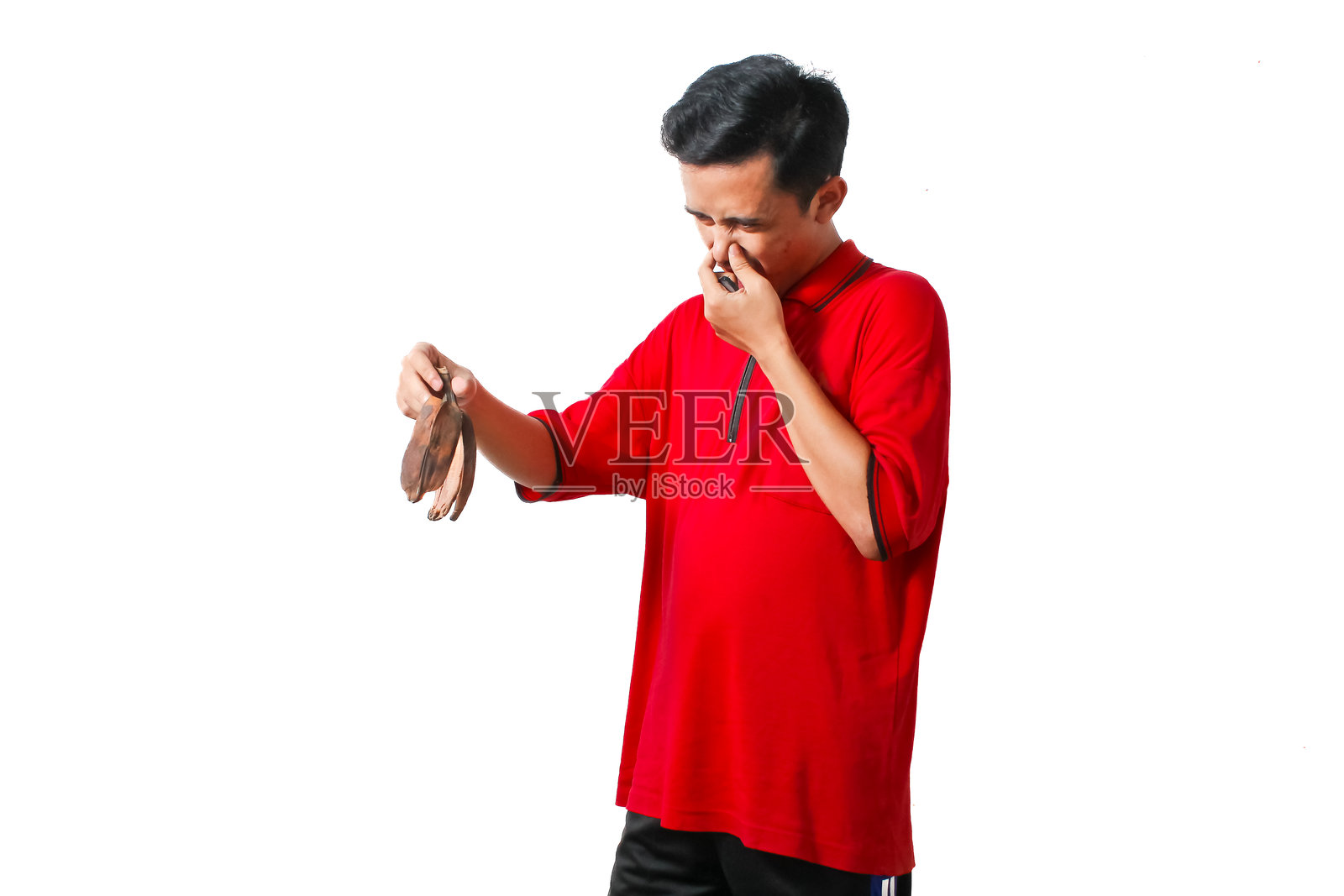 亚洲男子用手捂住鼻子，手里拿着一根臭香蕉皮。照片摄影图片