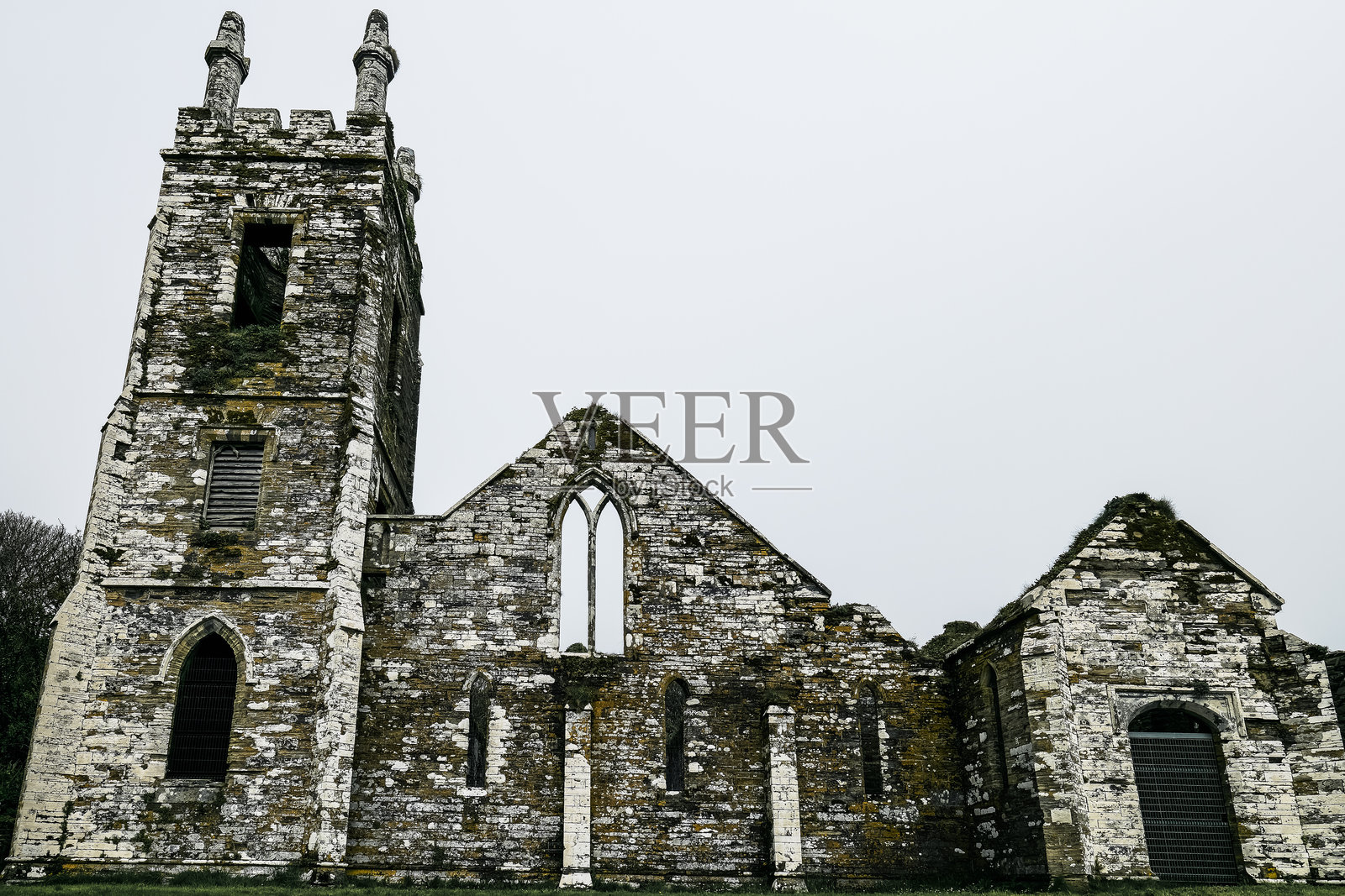 一座风化的石教堂遗迹在宁静的乡村风景中显得格外突出，展示着其历史建筑风格，周围是郁郁葱葱的草地，天空阴云密布。照片摄影图片