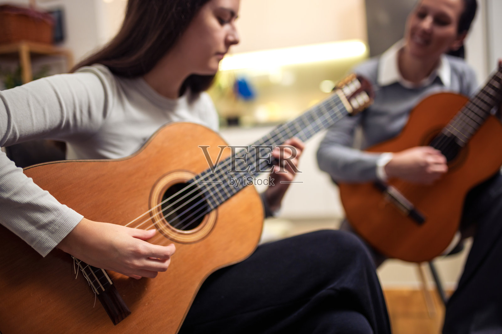 母女在家里弹吉他。母亲教女儿弹吉他。照片摄影图片