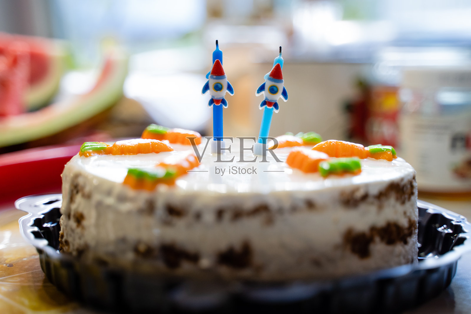 一个色彩鲜艳的生日蛋糕，上面装饰着可爱的火箭形蜡烛，并巧妙地用新鲜胡萝卜点缀，增添了它的魅力。照片摄影图片