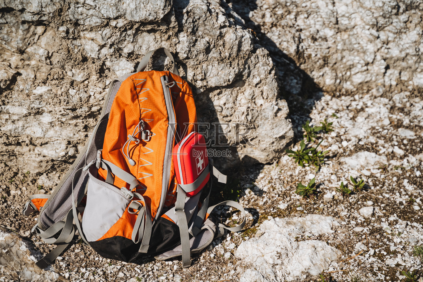 一款鲜艳的橙色登山背包静静地放在崎岖的岩石地形上，展现出大自然的美丽与探险精神。照片摄影图片
