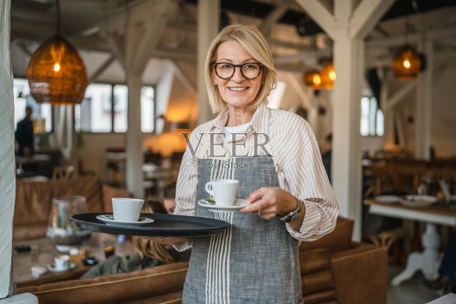 成熟的女服务员穿着围裙，提供一杯美味的咖啡照片摄影图片