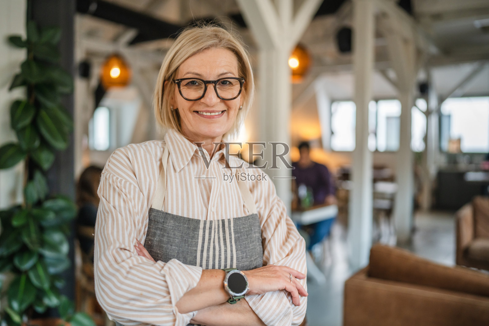 一位快乐的成熟的女性站在餐厅里，双臂交叉。照片摄影图片