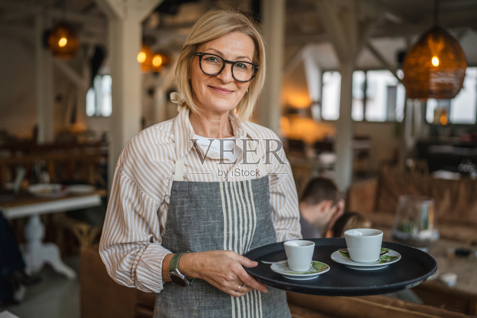成熟的女服务员穿着围裙，提供一杯美味的咖啡照片摄影图片