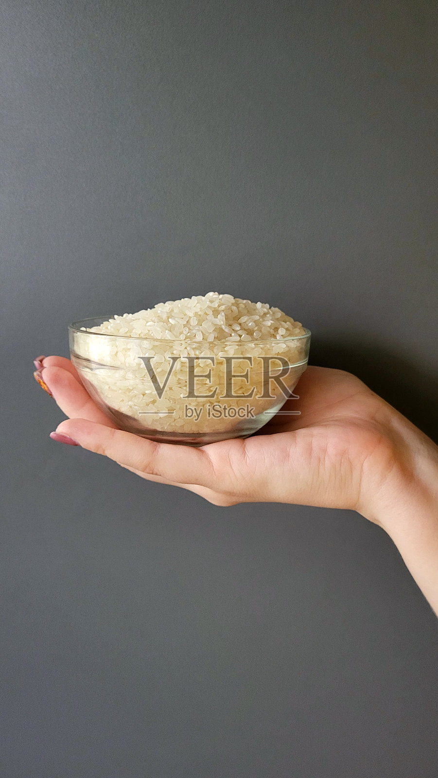 女人手中侧视的米饭盘。灰色背景下的玻璃碗中的米粥，侧视图。照片摄影图片