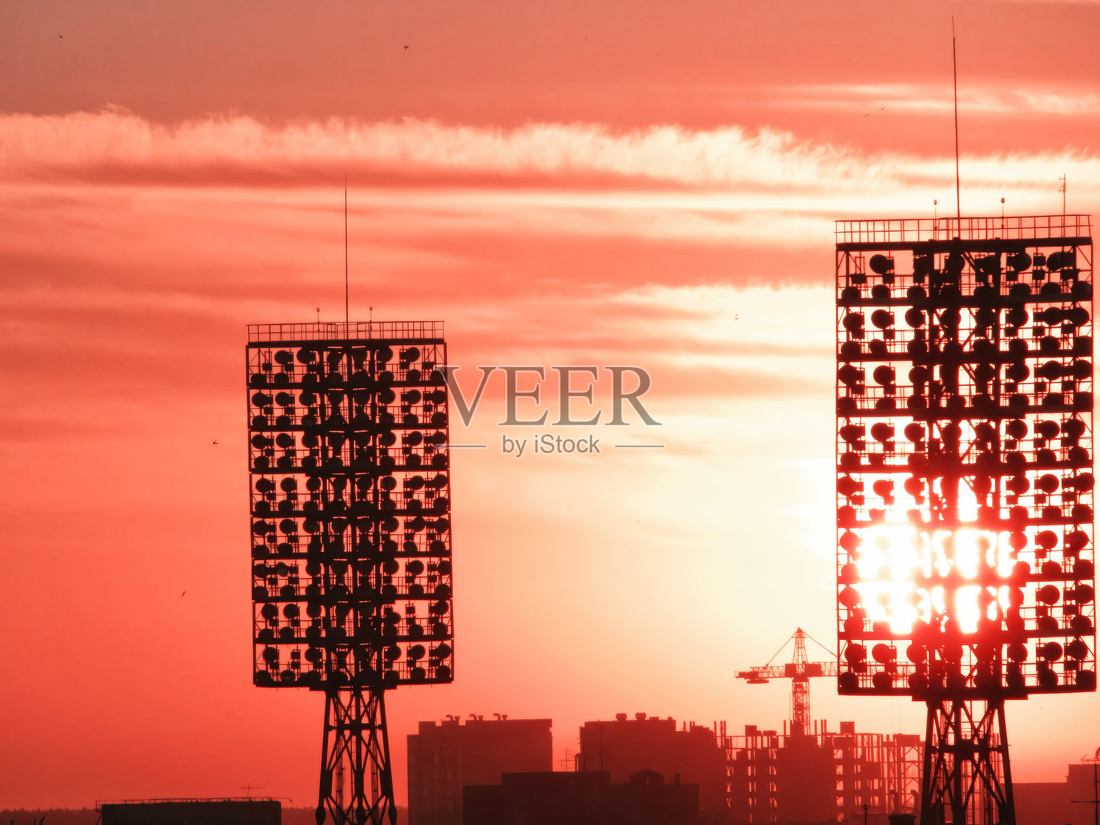 两座体育场灯塔在火红的日落天空中高耸入云。照片摄影图片