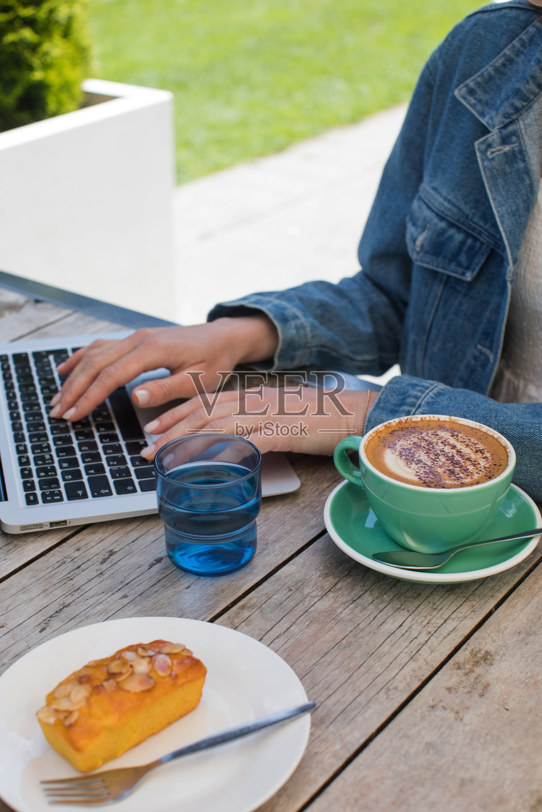在咖啡馆桌子旁，手握咖啡杯的女性正在用笔记本电脑打字照片摄影图片