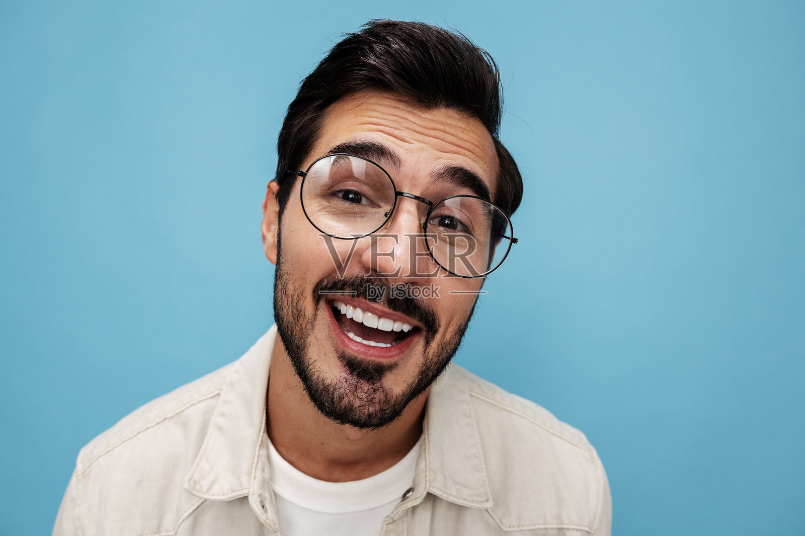 棕发男士近距离肖像，佩戴眼镜微笑露齿，背景为蓝色，穿着白色T恤，留有空白空间。照片摄影图片