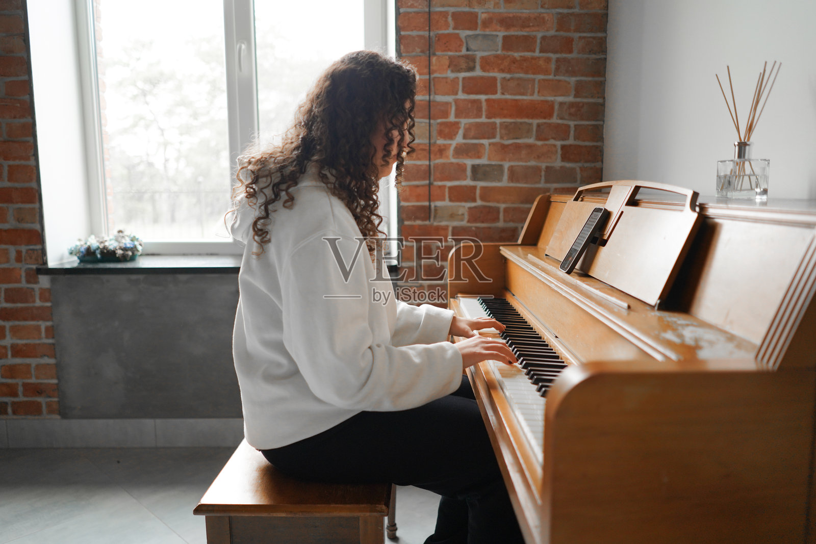 一位卷发女性坐在钢琴前，享受着音乐。照片摄影图片
