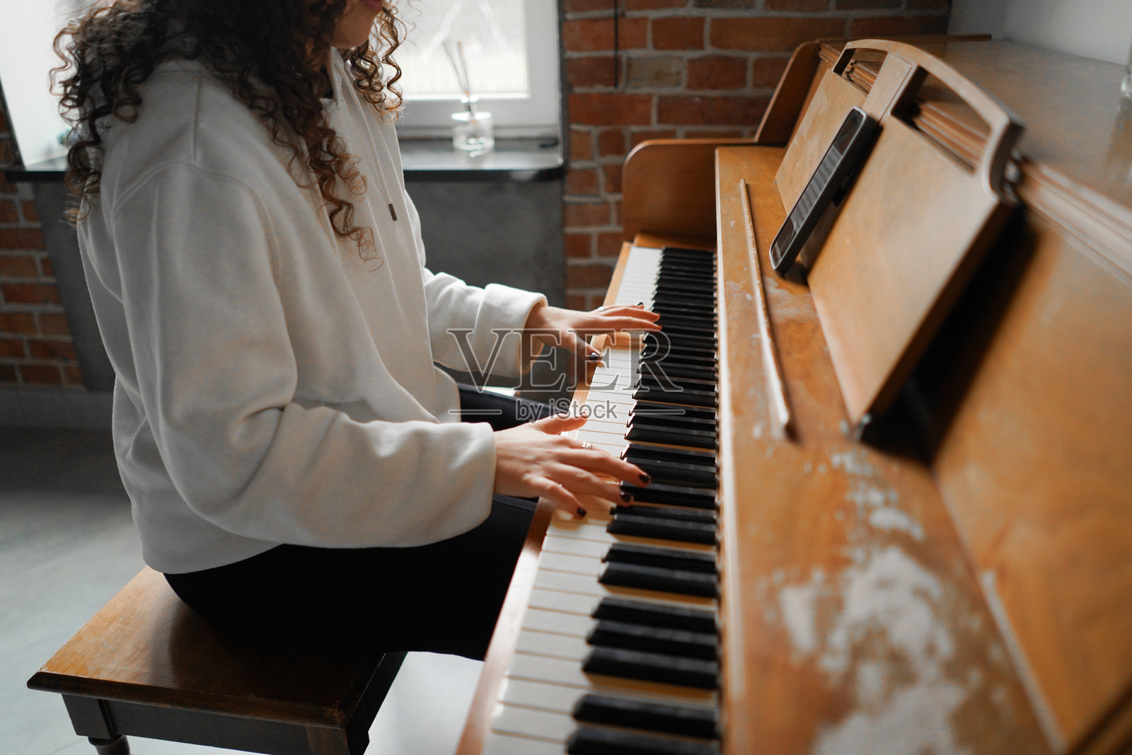 一位卷发女性坐在钢琴前，享受着音乐。照片摄影图片