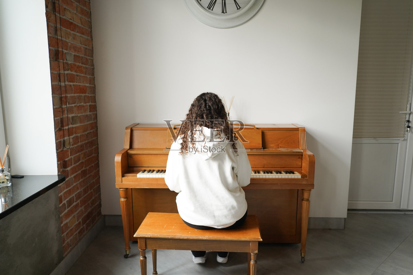 一位卷发女性坐在钢琴前，享受着音乐。照片摄影图片