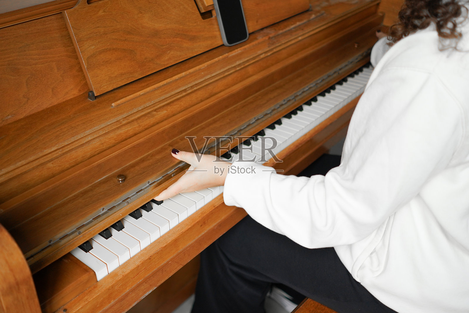 一位卷发女性坐在钢琴前，享受着音乐。照片摄影图片