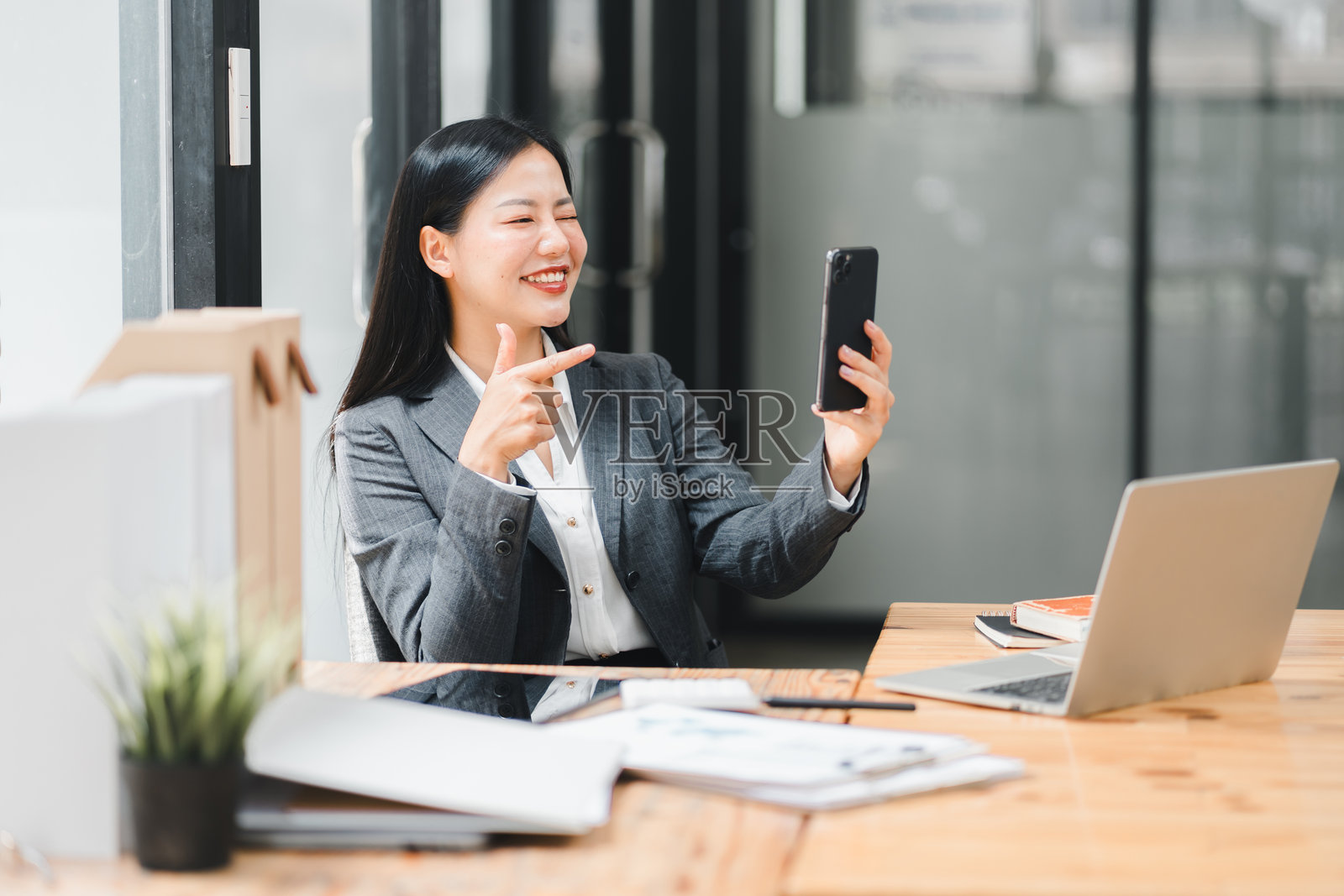 一位女商人在办公室环境中微笑着通过智能手机进行视频通话。照片摄影图片