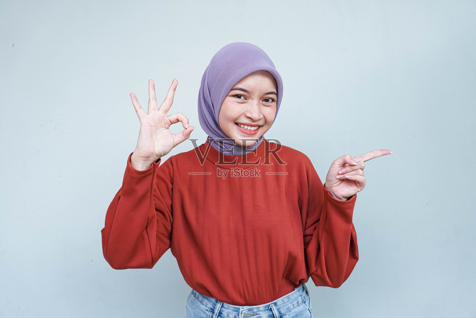 穿着红色毛衣的美丽微笑亚洲女性做出“好的”手势并指向或展示手势。照片摄影图片