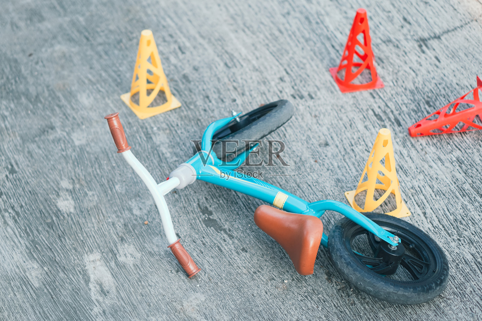 特写绿色托斯卡平衡车和训练用的锥形标志，遗弃在混凝土地面上。适合幼儿的安全骑行训练。照片摄影图片