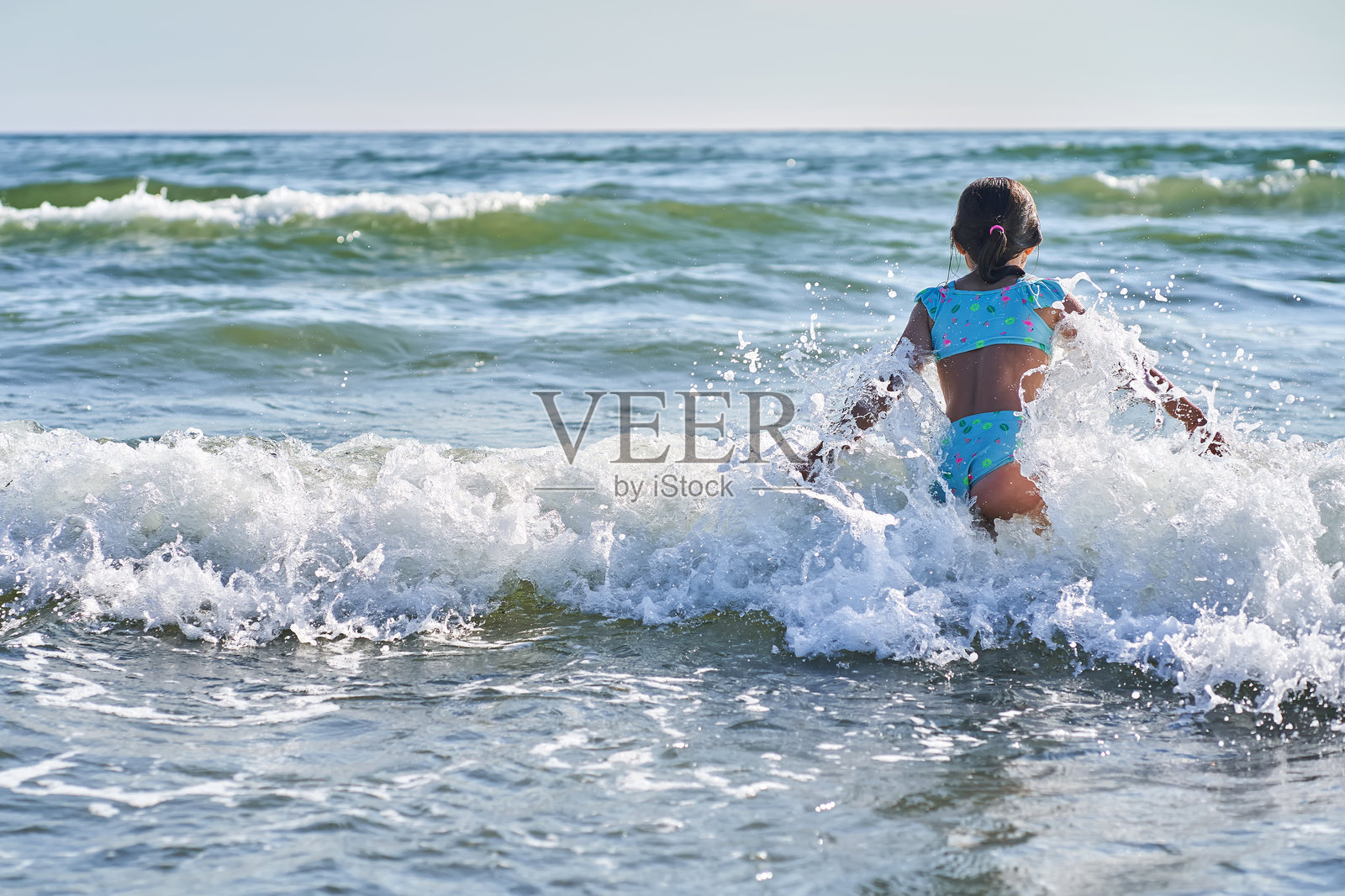 一个8岁的小女孩穿着泳衣在海浪中玩得很开心。照片摄影图片