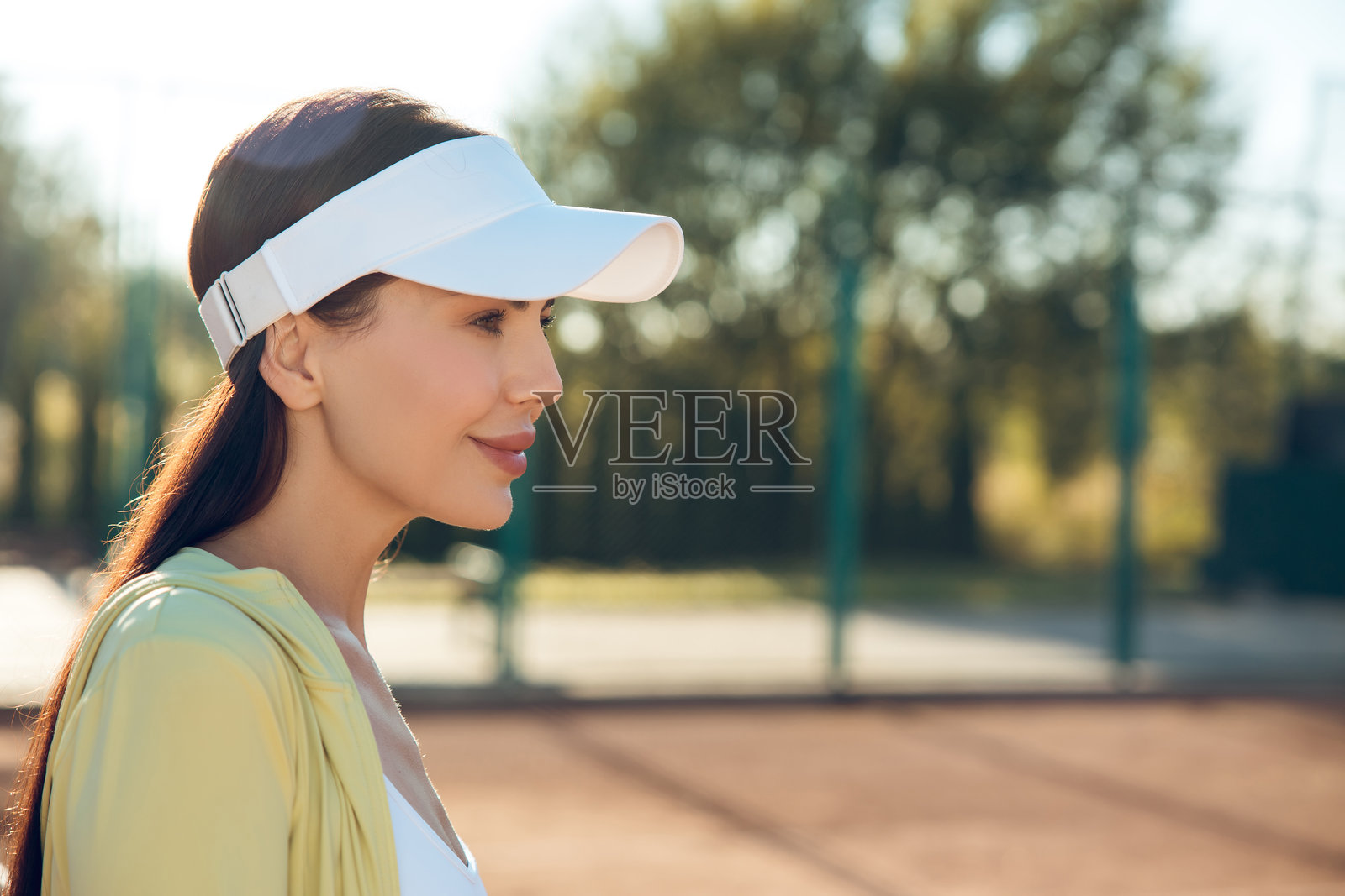 可爱的女性网球运动员戴着白色帽子，感到快乐并微笑。照片摄影图片