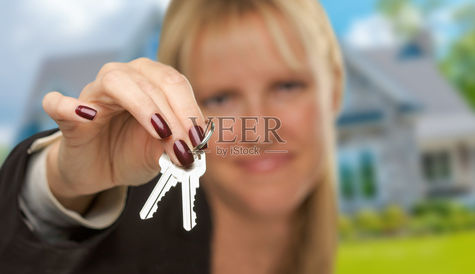 女性房地产经纪人在新房前展示房钥匙，重点在钥匙上。照片摄影图片