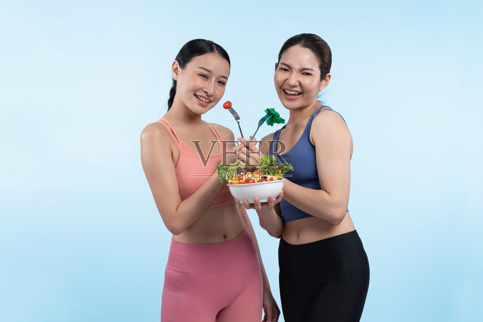 穿着运动服的亚洲女性在孤立背景下手持沙拉碗。充满活力照片摄影图片