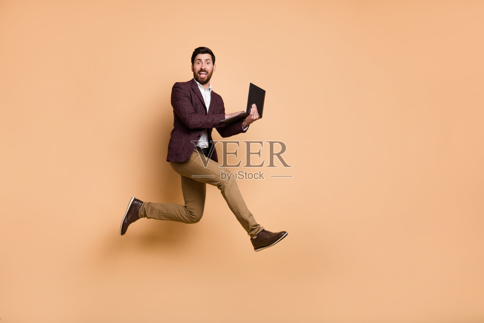 全身像的兴奋精力充沛的商人急匆匆地参加在线会议，背景为米色。照片摄影图片