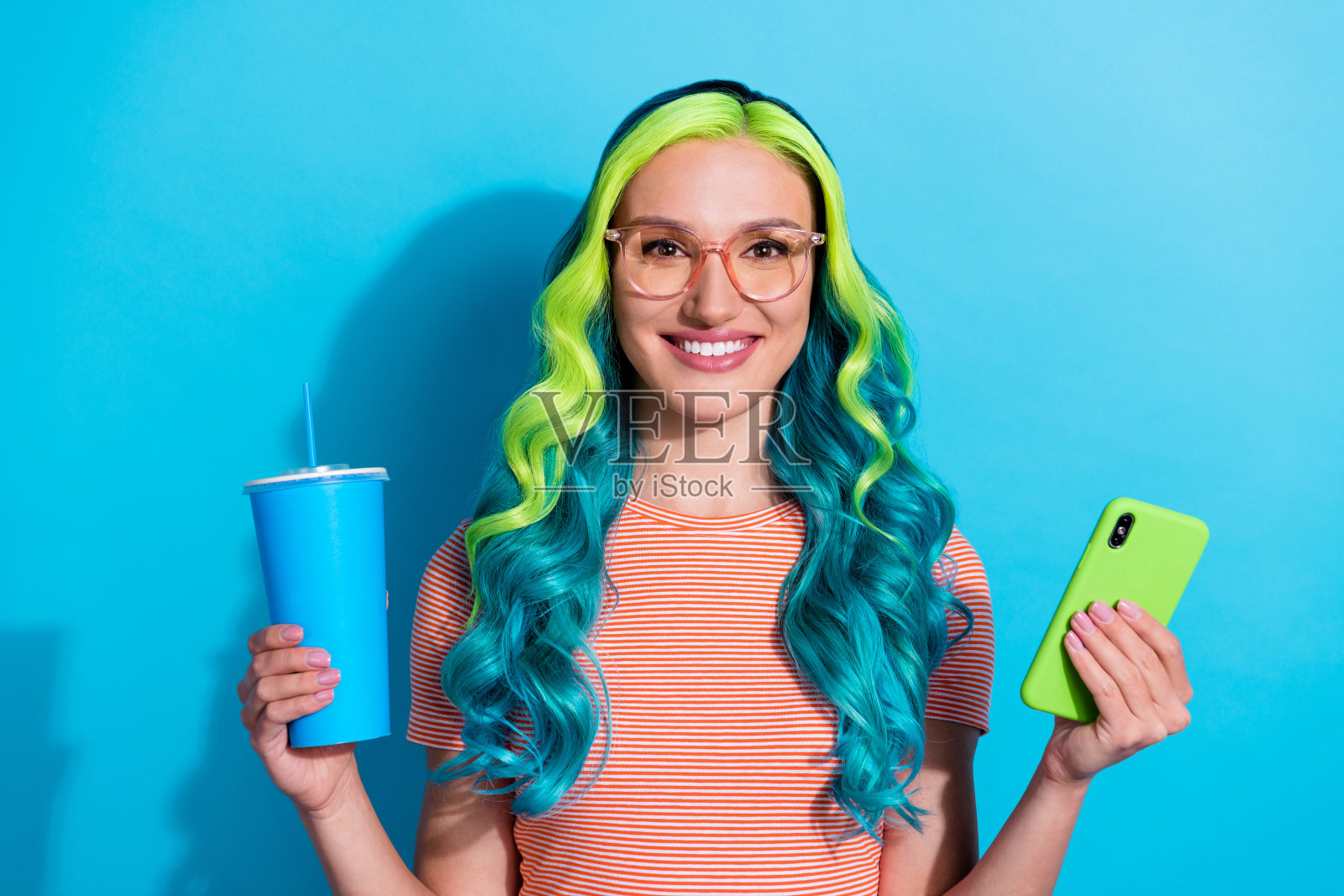 年轻迷人的女性，拥有独特的海蓝色头发，在蓝色背景下冲浪社交媒体。照片摄影图片