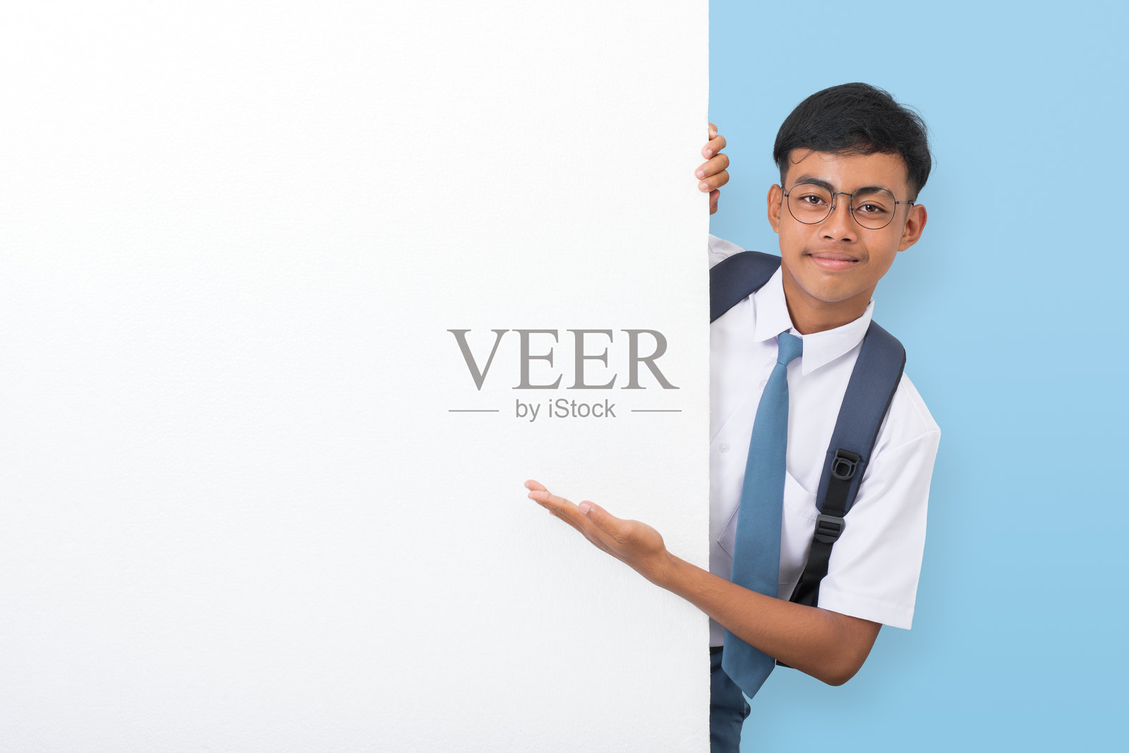 印尼高中生站在白色墙壁后面，指向墙壁。设计、样板和广告的空白空间。照片摄影图片