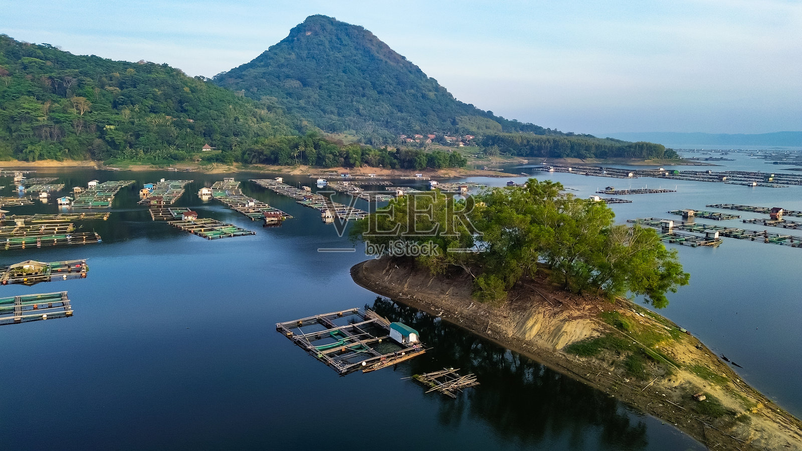 在宁静的水域中，环绕着郁郁葱葱的山丘，漂浮的鱼塘进行鱼类养殖。贾蒂卢赫水库照片摄影图片