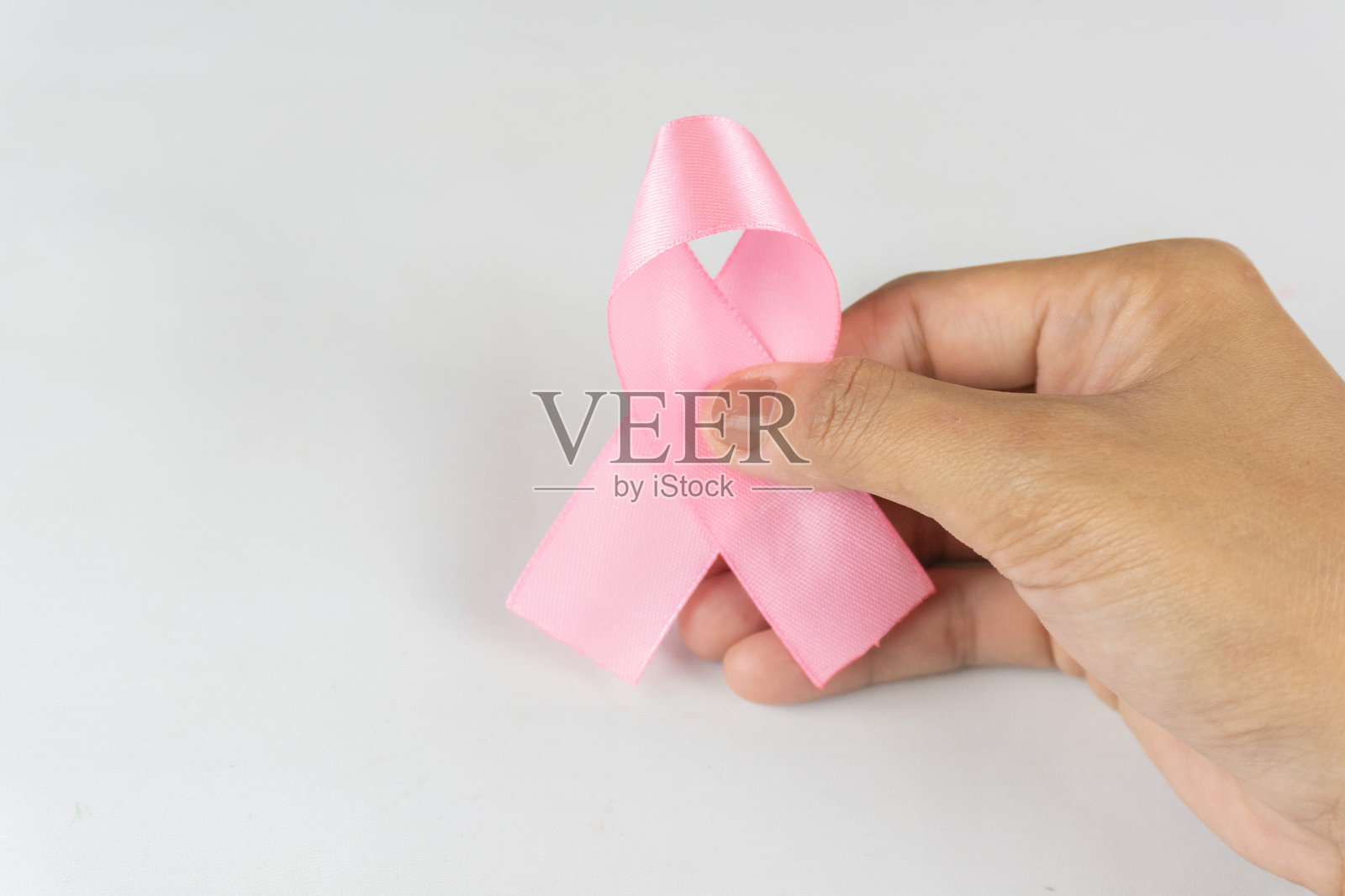 一只手握着粉色丝带，背景为白色。这是乳腺癌意识的象征，癌症意识月。照片摄影图片