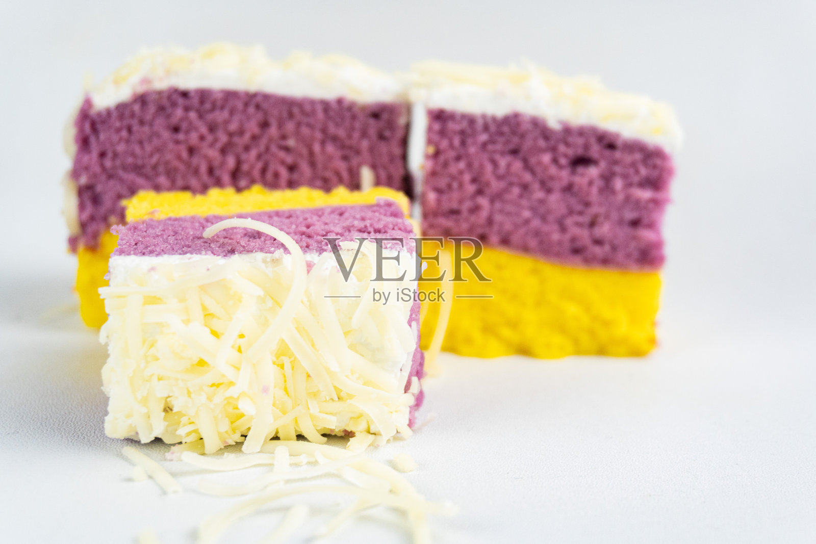 紫色和黄色的蛋糕块上覆盖着奶酪片，孤立在白色背景上。照片摄影图片