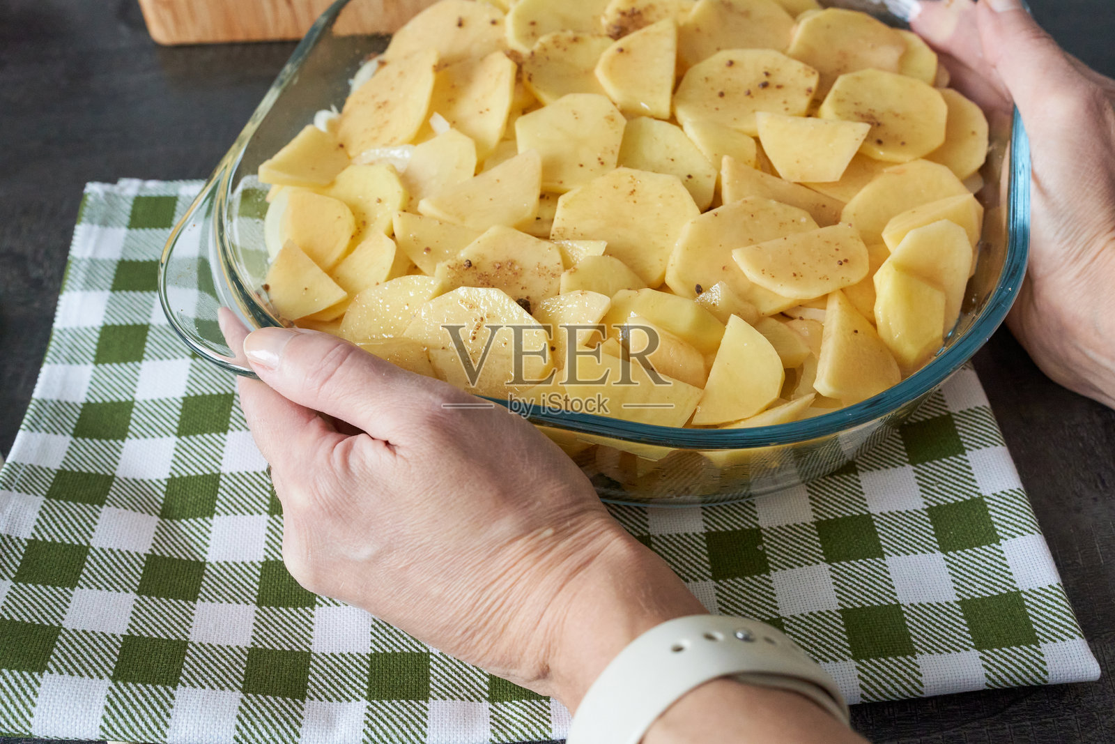 女人的手拿着一个装有土豆片的玻璃碗。正在烹饪一道土豆菜肴。照片摄影图片