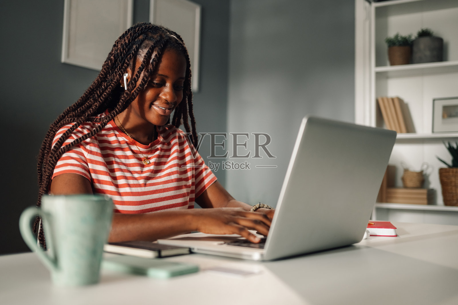 年轻女性在家工作，戴着耳机，正在笔记本电脑上打字照片摄影图片